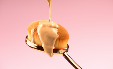 Makeup liquid foundation pouring on make-up brush, closeup. Foundation beauty facial cosmetics,...