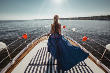 Woman in flying beautiful blue dress on a boat. Wide view on front of yacht. Back view