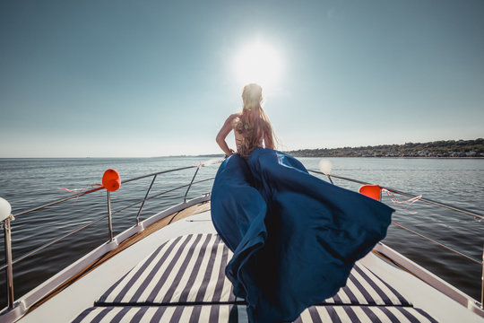 Woman in flying beautiful blue dress on a boat. Wide view on front of yacht. Back view