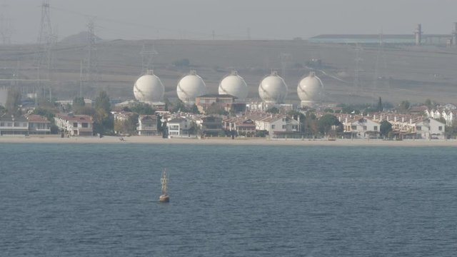 Liquefied gas storage behind cottages and beach on sea shore in sunny day