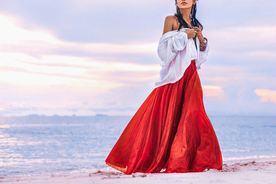 beautiful young stylish boho woman walking on the beach at sunset