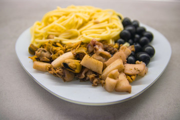 white plate on a gray kitchen table with spaghetti with black olives and seafood close up
