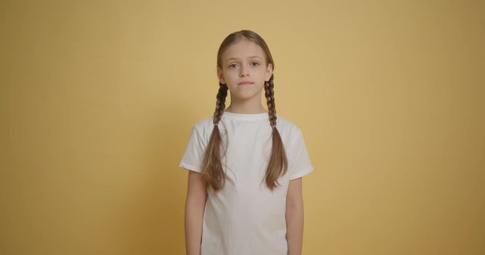 Girl with braids looking to the camera at yellow wall background slow motion