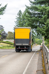 Big rig day cab semi truck with box trailer driving on the city street for goods delivery