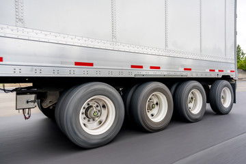 Big rig semi truck transporting four-axle semi trailer for transporting heavy loads running on the road