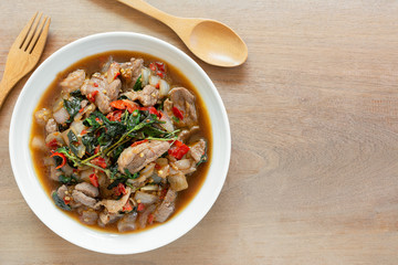 top view of stir fried duck meat with holy basil in a ceramic dish on wooden table. hot and spicy thai style food menu.