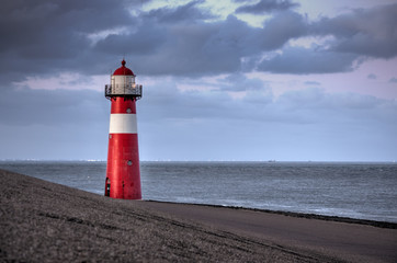 A red and white lighthouse at sea at dusk near Zeeland, Netherlands.