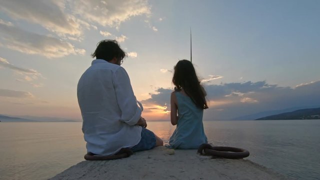 Rear view of little girl sitting on the edge of a dock and fishing with father Mediterranean Sea at sunset. Enjoying adventure in summer vacation
