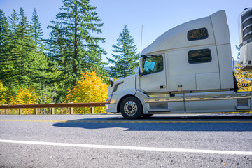 Fototapeta na wymiar Profile of big rig semi truck with refrigerator semi trailer running downhill on the autumn road
