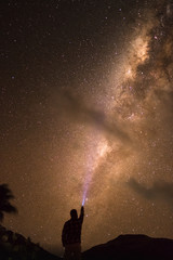 Fototapeta na wymiar Silhouette of a young man with a torch shining on a milky way visible on a beach in Fiji