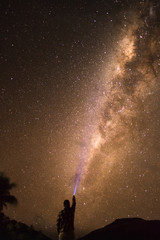Silhouette of a young man with a torch shining on a milky way visible on a beach in Fiji