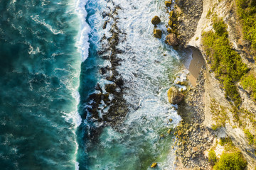 View from above, stunning aerial view of a rocky shore with a beautiful beach bathed by a rough sea during sunset, Nyang Nyang Beach (Pantai Nyang Nyang), South Bali, Indonesia.