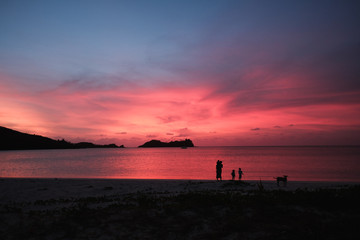 Malakati village, Fiji - 10/26/2019: Family walking on the beach, colourful sunset with palm trees...