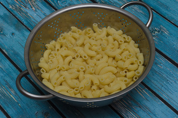 boiled italian pasta in aluminum colander on wooden blue background
