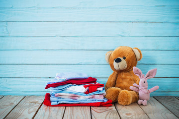 baby clothes and toy bear on old wooden background