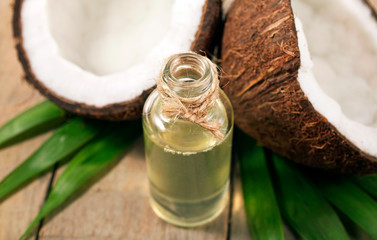Coconut on palm leaves with melted coconut oil in a glass bottle on wooden background. 