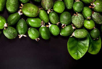 Fresh feijoa fruits (acca sellowiana, pineapple guava) and leaves isolated on a black background. Top view. Text space.