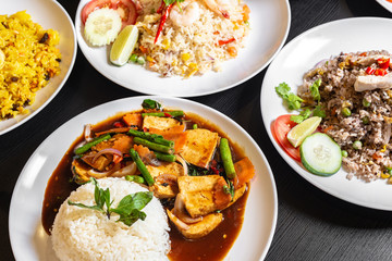 Variety of Thailand dishes on table. Stir-fried Mixed Vegetables Tofu with jasmine white rice, Olive fried rice, Thai Seafood, Pineapple fried rice in the background.