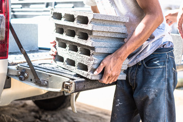 Worker moving heavy building materials from trunk car pickup. Construction male worker carry loading concrete block for house construction.