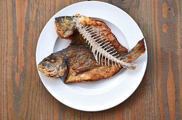Fried fish and fishbone on a white plate and wooden background.