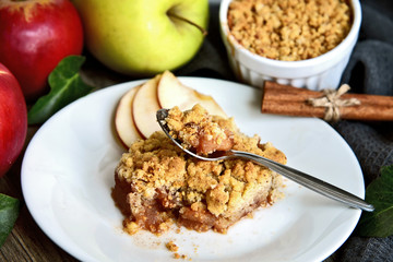 Apple crumble on with dish with spoon and fresh green and red apple with cinnamon stick on wooden floor. Easy and Basic dessert menu.