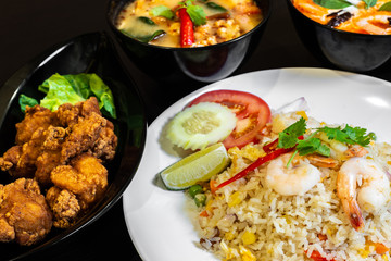 Thai seafood fried rice served with prawns, a plate of Fried Chicken Karaage, and two bowls of Tom Yum Soup in the background.
