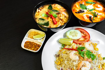 Thai seafood fried rice served with prawns in a white plate, and two bowls of Tom Yum Soup in the background.