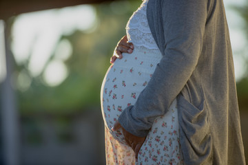 Young pregnant woman embracing her naked abdomen with hands outdoor. Big belly on the third...
