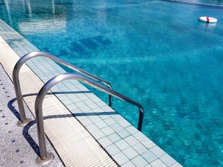 Selective focus blurred shot of swimming pool in summer season hot sunny day. With safety life ring and handrail step. Standard protection equipment of pool for prevent accident in emergency case.