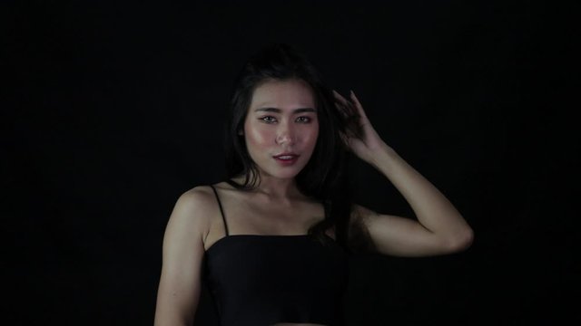 Asian Lady in black with long hair smile then touch hair to sleek up on black background in studio
