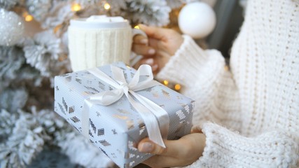 Fototapeta na wymiar Christmas. Close-Up Of Female Hands Holds Xmas Present And Cup Of Hot Chocolate.
