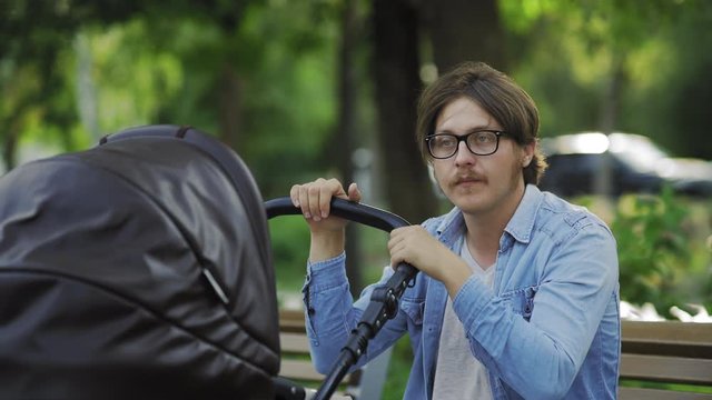 Tired father falling asleep during relax time with baby in park, swinging stroller