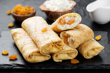 Thin pancakes or crepes stuffed with cottage cheese and raisins on black background. 