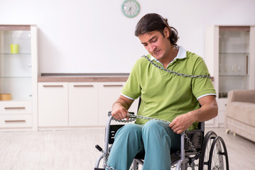 Young male invalid in wheel-chair suffering at home