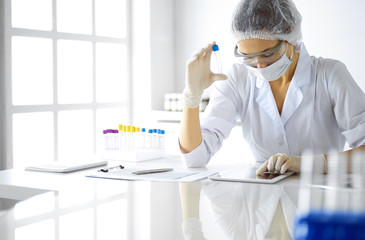 Professional female scientist in protective eyeglasses researching tube with reagents in laboratory. Concepts of medicine and research