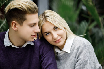 Cute blond guy and girl sitting among tropical plants in big store. Shop for decor