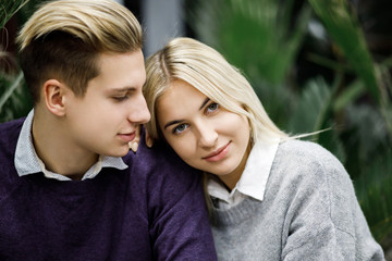 Fototapeta premium Cute blond guy and girl sitting among tropical plants in big store. Shop for decor