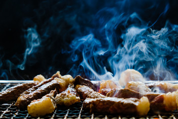 raw meat beef steak sliced bbq grilling on rack charcoal stove with smoke and fire flame on black background.
