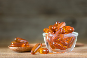 Fish oil pills in a glass bowl on wooden table with dark background, vitamin D and omega 3 source...