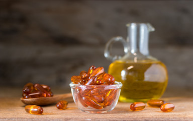 Fish oil pills in a glass bowl on wooden table with dark background, vitamin D and omega 3 source...