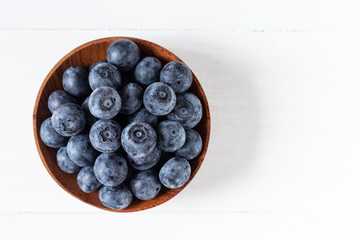 Blueberries in a wooden bowl on white table in top view or flat lay, fresh fruit