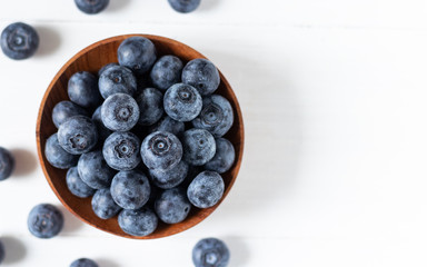Blueberries in a wooden bowl on white table in top view or flat lay, fresh fruit