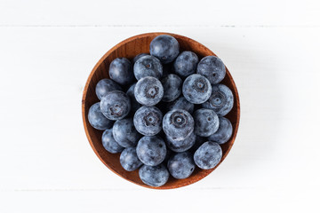 Blueberries in a wooden bowl on white table in top view or flat lay, fresh fruit