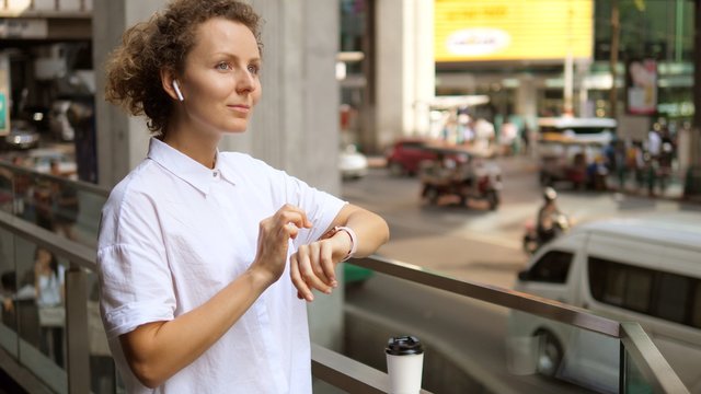 Woman Using Smartwatch In Wireless Earphones In City