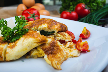 Traditional omelet with vegetables, spinach, tomatoes and herbs on a wooden table in a restaurant. Classic european breakfast. Fried eggs with milk and cheese. Soft focus.