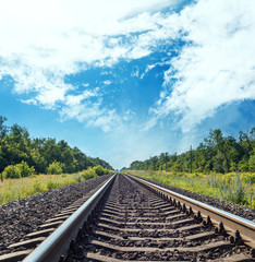 Fototapeta na wymiar one railroad to horizon in green meadow and blue sky with clouds