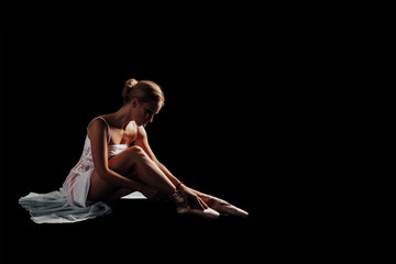 Fototapeta na wymiar Graceful ballet or gymnast sitting on a black background wears shoes - pointe shoes. dancer in a white dress. Isolated. Dancer posing in Studio with copy space. black background 