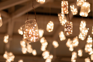 Jars hanging from the ceiling of the bar with warm led lights inside. - Powered by Adobe