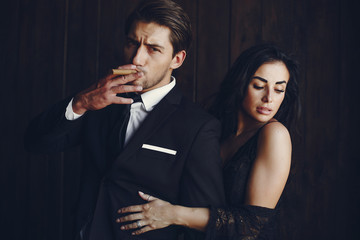 Elegant man in a black suit. Couple at home. Hot woman in a black underwear. Male with cigar