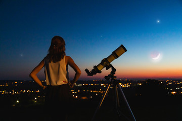 Astronomer with a telescope watching at the stars and Moon with blurred city lights in the...